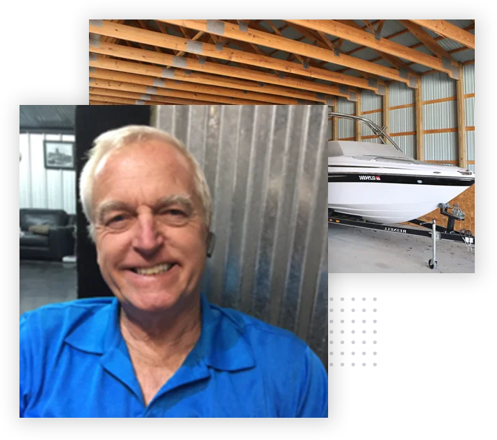 Smiling older man in blue shirt sits indoors; a white and black boat is stored in a metal garage behind him.