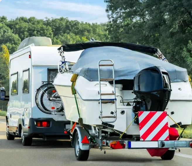 A motorhome towing a covered boat on a trailer with a bicycle mounted on the back, driving on a road.